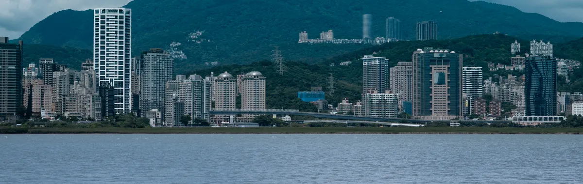 Stunning view of New Taipei City's urban skyline against lush green mountains and a serene water body.