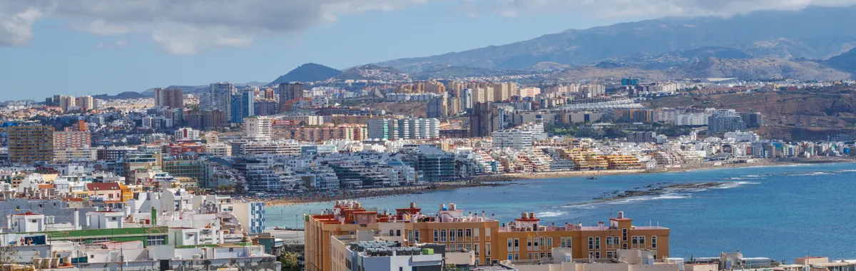 A scenic view of Las Palmas de Gran Canaria's cityscape and coastline under a blue sky.