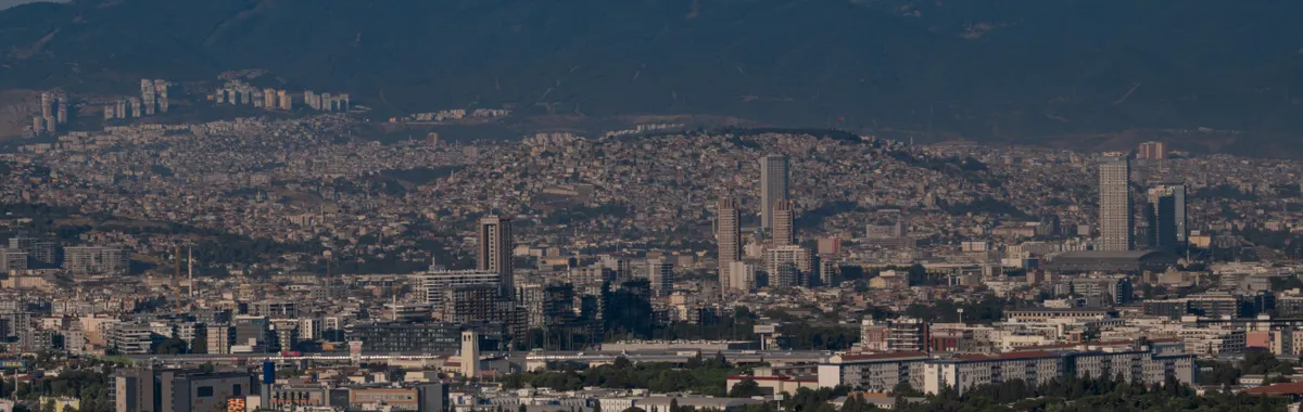 Aerial view of Izmir, Türkiye, showcasing cityscape and mountainous backdrop under a clear blue sky.
