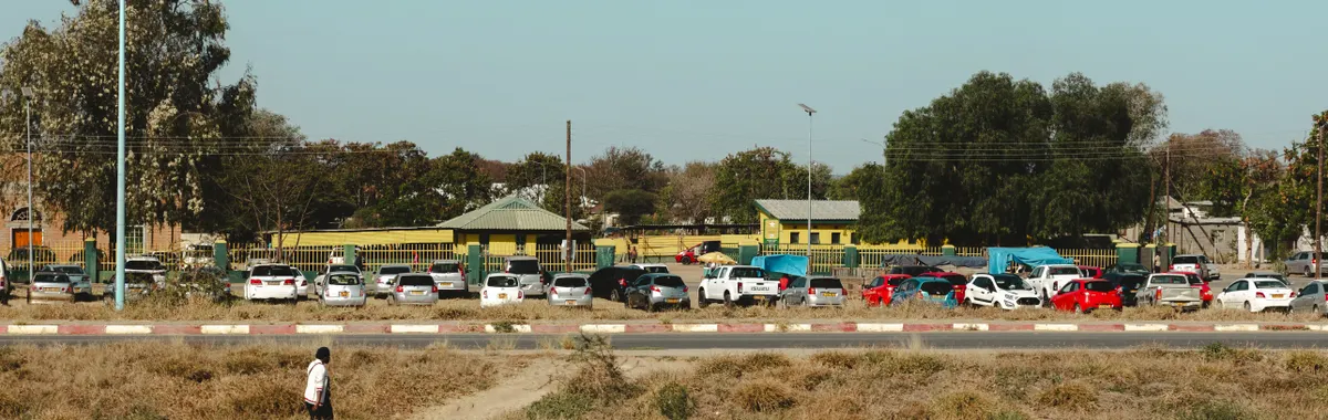 View of Francistown's urban landscape showcasing parked cars and a person walking in a grassy area.