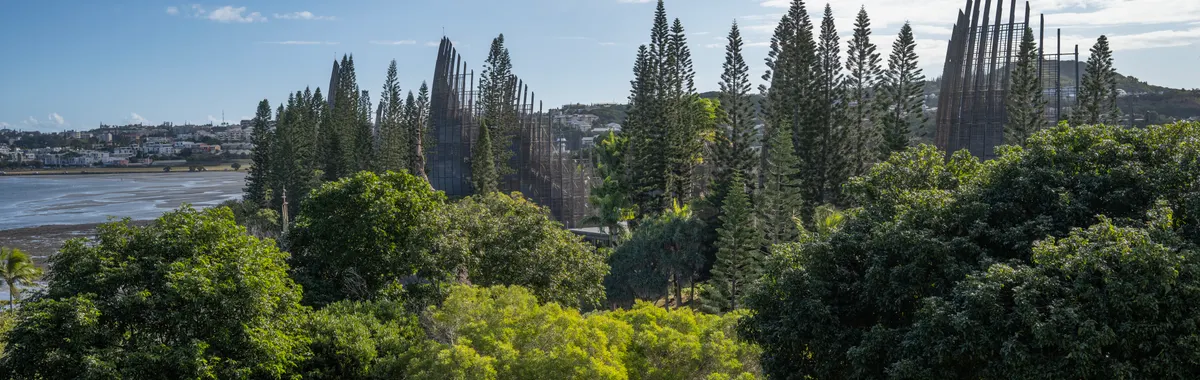 A scenic view of the Tjibaou Cultural Center with lush greenery and cloud-streaked sky in Nouméa.