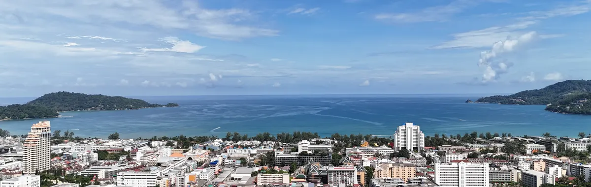 Stunning aerial view of Patong Beach in Phuket, Thailand, with blue skies and cityscape.