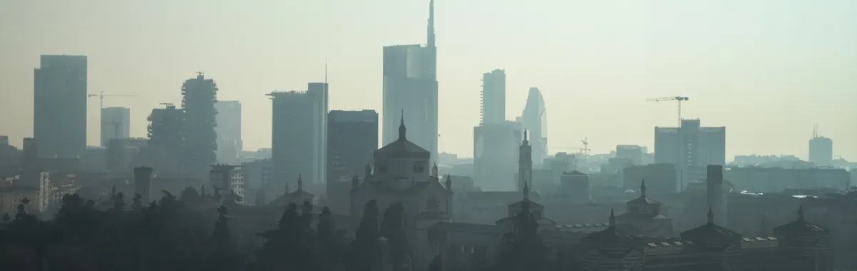 A foggy view of the Milan cityscape with modern skyscrapers and historic architecture.