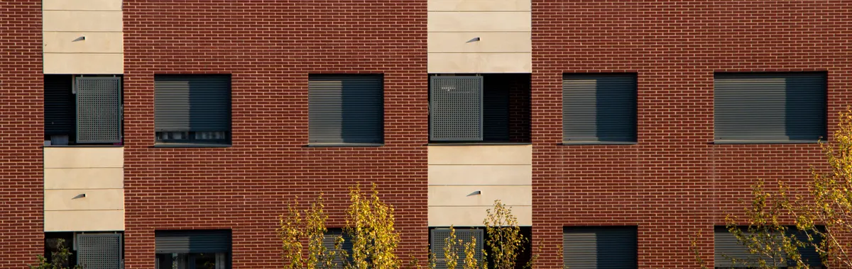 Close-up of a brick and concrete residential building facade in Logroño with symmetrical windows and trees below.