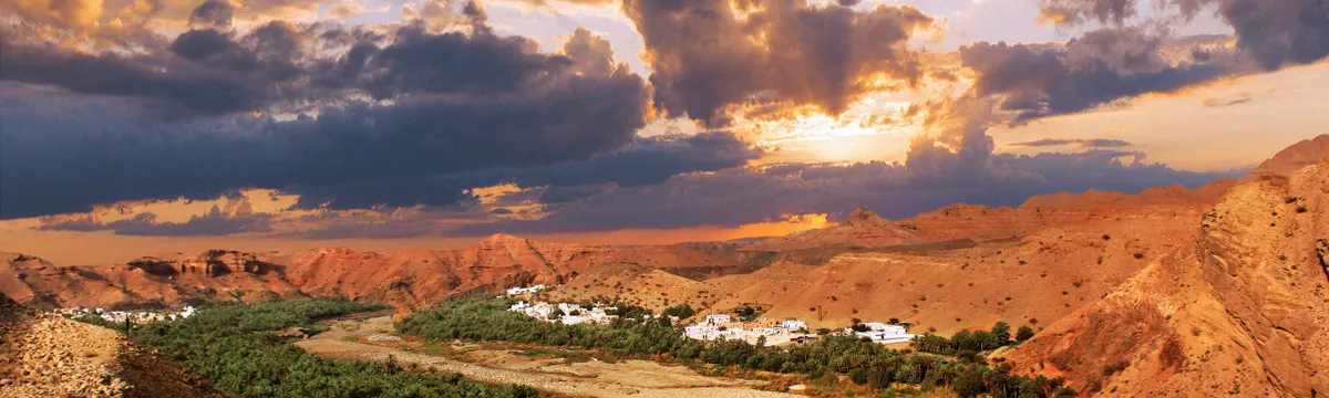 עומאן: Breathtaking view of a dramatic sunset illuminating Oman's rugged terrain with vibrant colors.