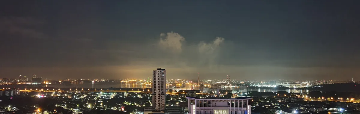 A vibrant night view of the Johor Bahru skyline with illuminated city lights and clear sky.