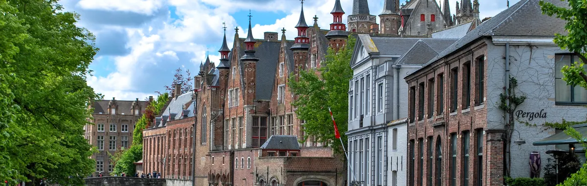 Charming canal scene in Brugge, Belgium showcasing historic architecture and a tour boat on a sunny day.
