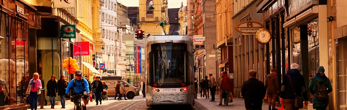 Urban street scene in Linz, Austria with tram, cyclists, and pedestrians.