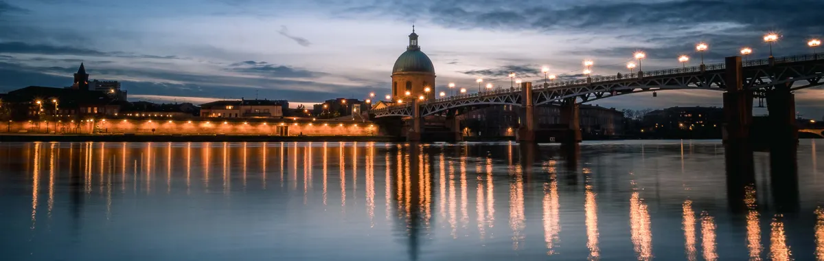 Serene twilight view of Pont Saint-Pierre and Garonne River in Toulouse, France, with city lights reflecting in the water.