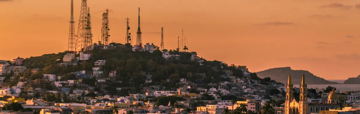A breathtaking view of Mazatlán's skyline and cathedral at sunset with vibrant orange hues.