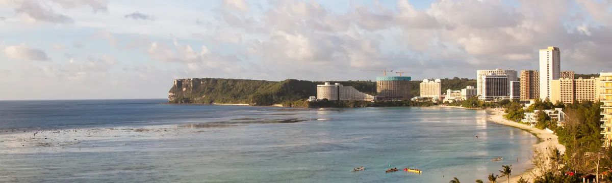 גואם: A beautiful aerial view of a tropical beach and cityscape in Guam, showcasing the coastline and modern architecture.