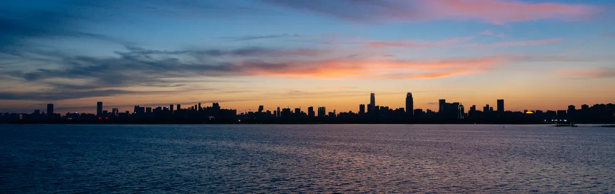 The serene skyline of Wuhan silhouetted against a twilight sky over a calm river.