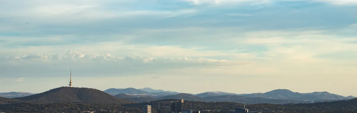 A scenic aerial view of Canberra highlighting Telstra Tower and surrounding landscape under a blue sky.