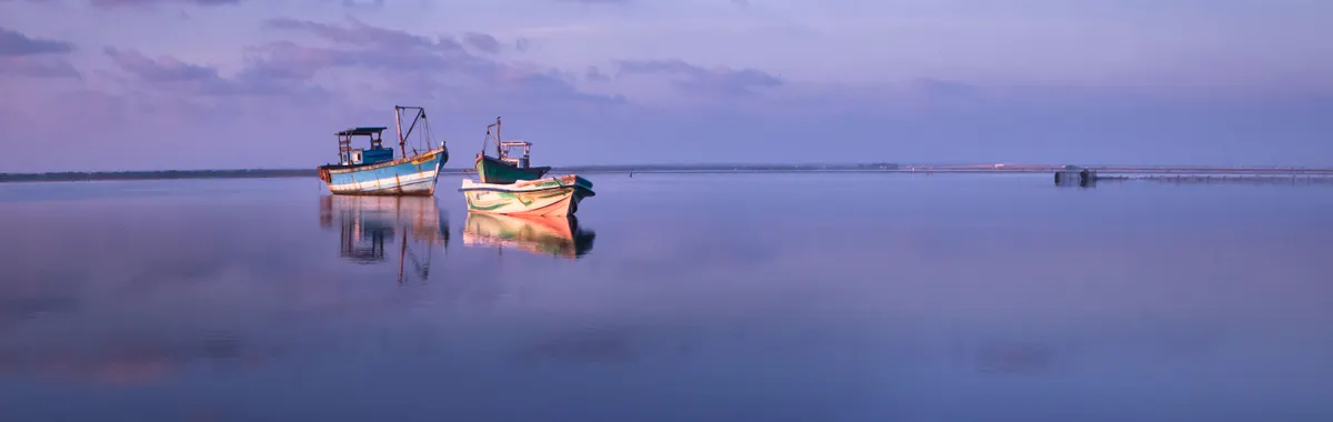 Calm waters and fishing boats under a pastel sky at sunset in Jaffna, Sri Lanka.