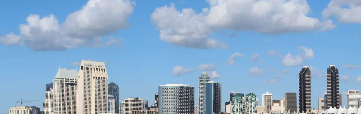 View of San Diego skyline with tall buildings and a ship on a bright day.