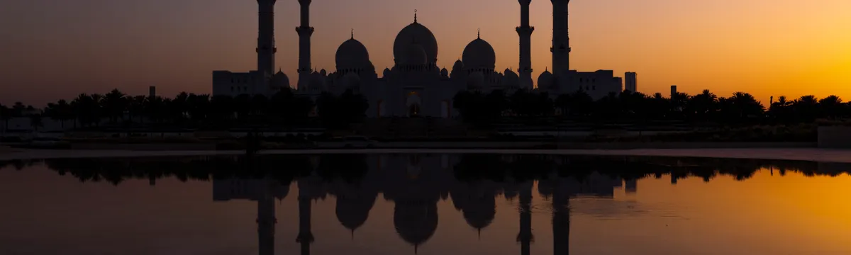 איחוד האמירויות הערביות: Silhouette of Sheikh Zayed Grand Mosque reflecting in water during a vibrant sunset in Abu Dhabi.