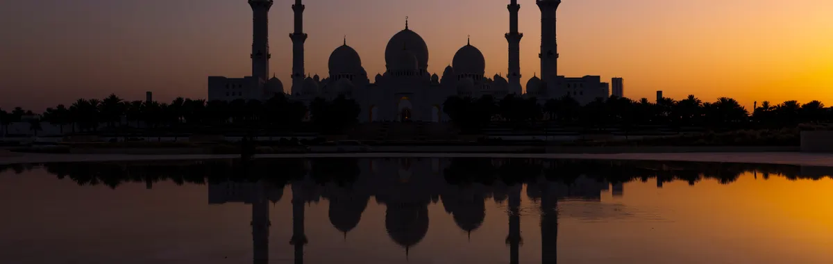 איחוד האמירויות הערביות: Silhouette of Sheikh Zayed Grand Mosque reflecting in water during a vibrant sunset in Abu Dhabi.
