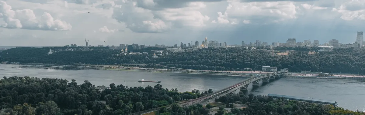 A stunning aerial view of Kyiv's skyline and the Dnipro River, featuring a prominent bridge, amidst lush greenery.