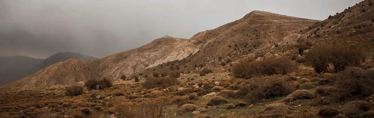 איראן: A rugged mountainous landscape under a cloudy sky in Tehran, offering a dramatic and earthy scene.