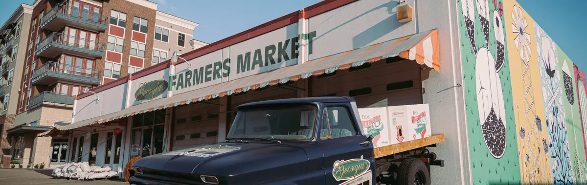 A classic truck parked outside a colorful farmers market in Plano, Texas, under a clear sky.