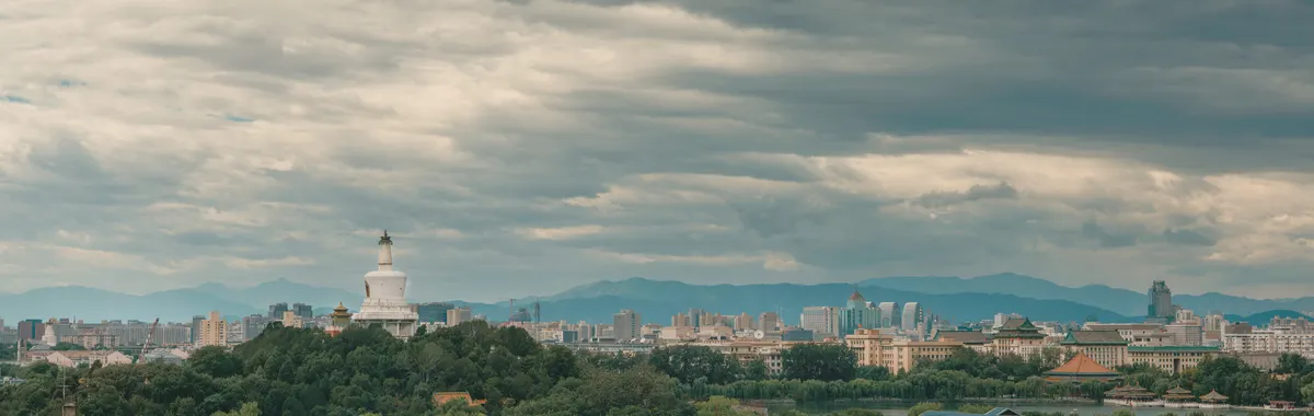 Panoramic view of Beijing with the iconic White Dagoba stupa under a cloudy sky.