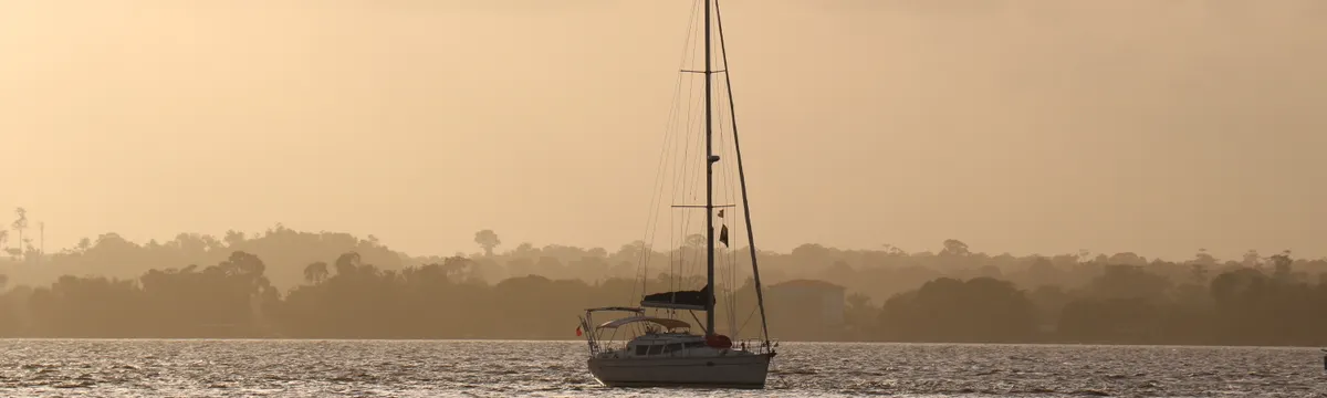 גיאנה הצרפתית: A serene sailboat drifting on the ocean against a warm sunset in French Guiana.